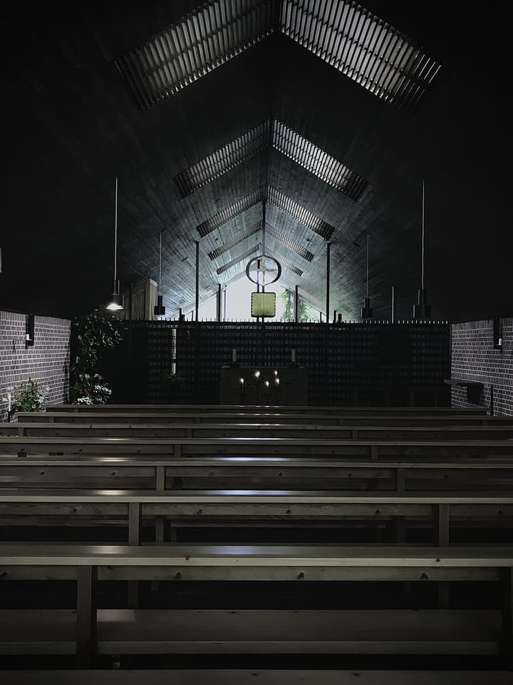 Looking down a chapel nave of wooden benches toward an altar under a high wooden ceiling.