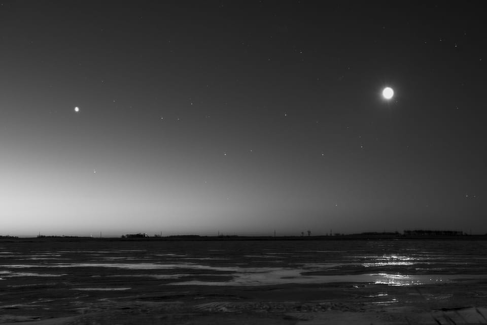 Black-and-white night over frozen ground, with the moon at right and a lesser light at left.