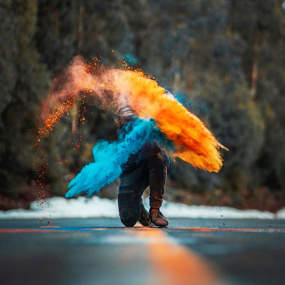 A kneeling figure on a winter road inside a burst of orange and blue powder.