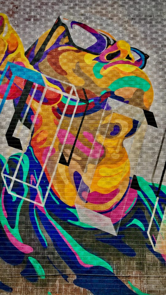 A colorful painted face on a brick wall, photographed as a still, not as a painting by this artist.